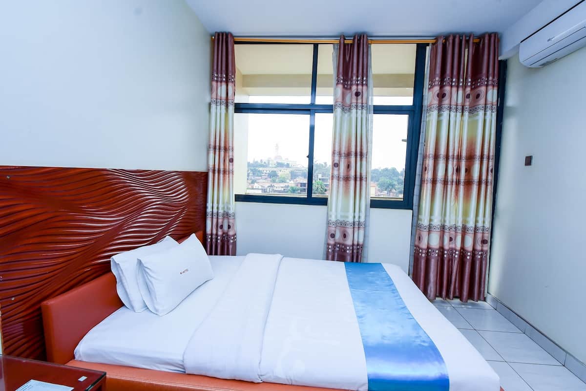 Une chambre d’hôtel avec un lit, une tête de lit en bois, une fenêtre avec des rideaux et un appareil de climatisation.