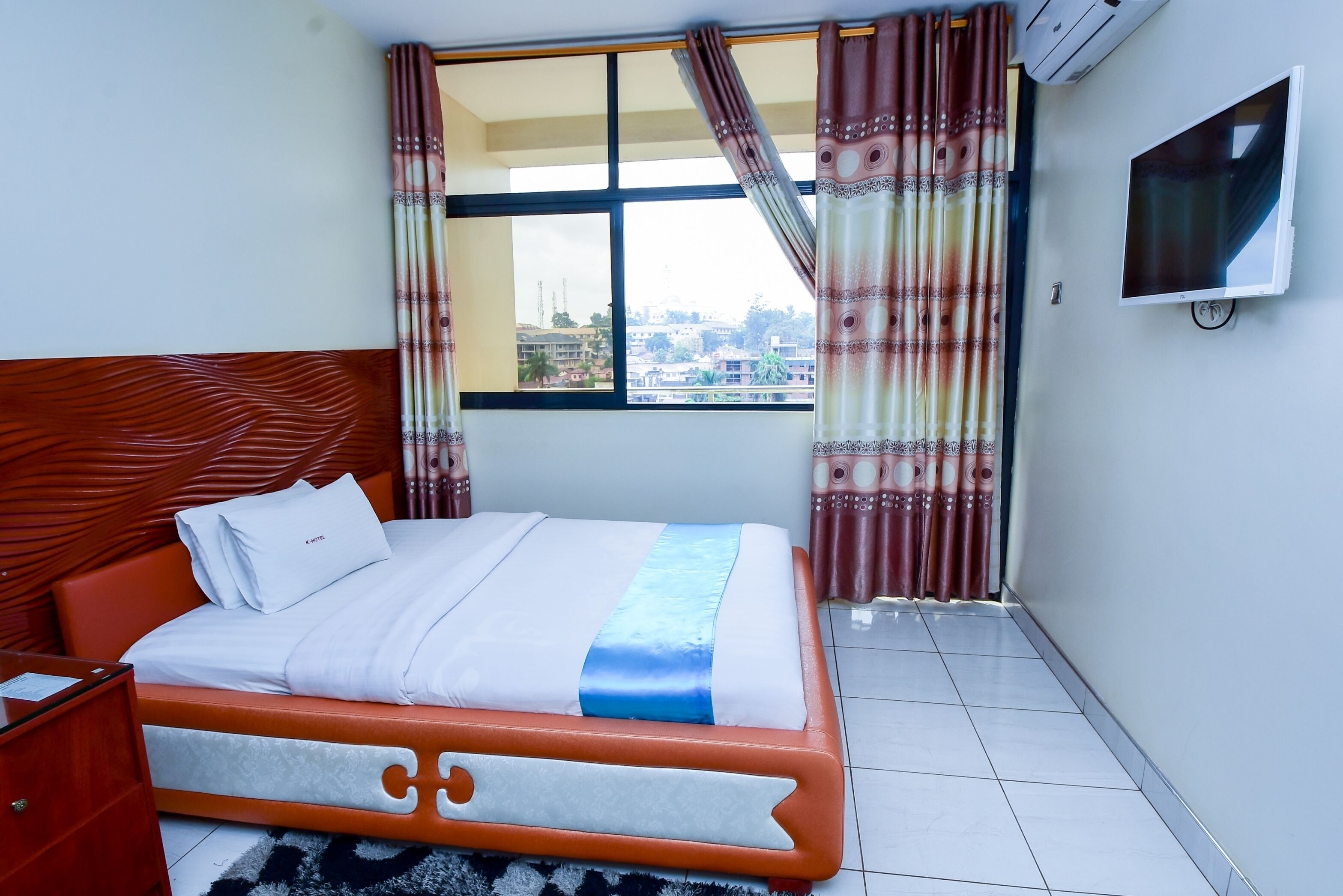 A hotel room with a bed, a TV, and a window with curtains.