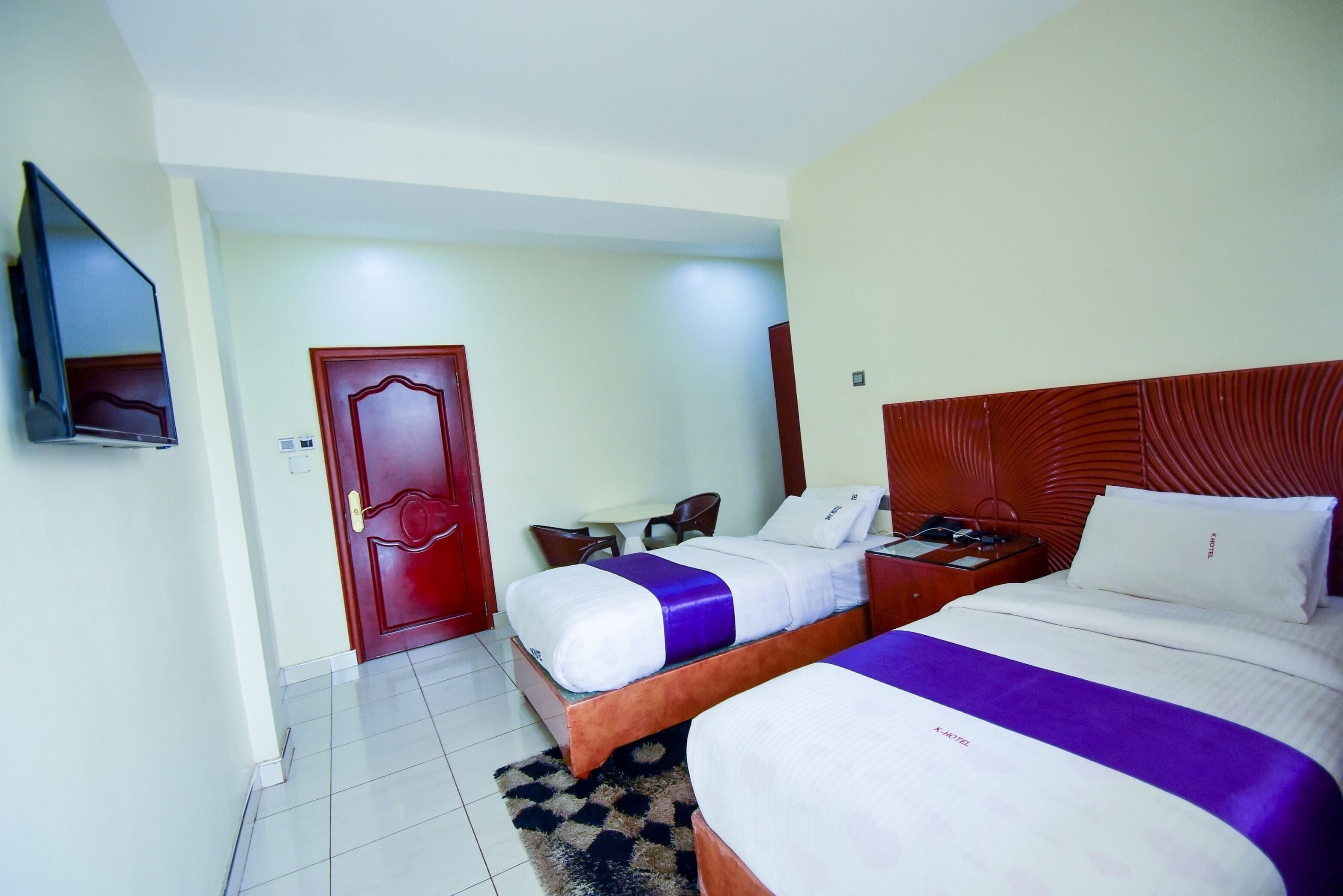 A hotel room with two beds, a TV, a wooden headboard, and a door.