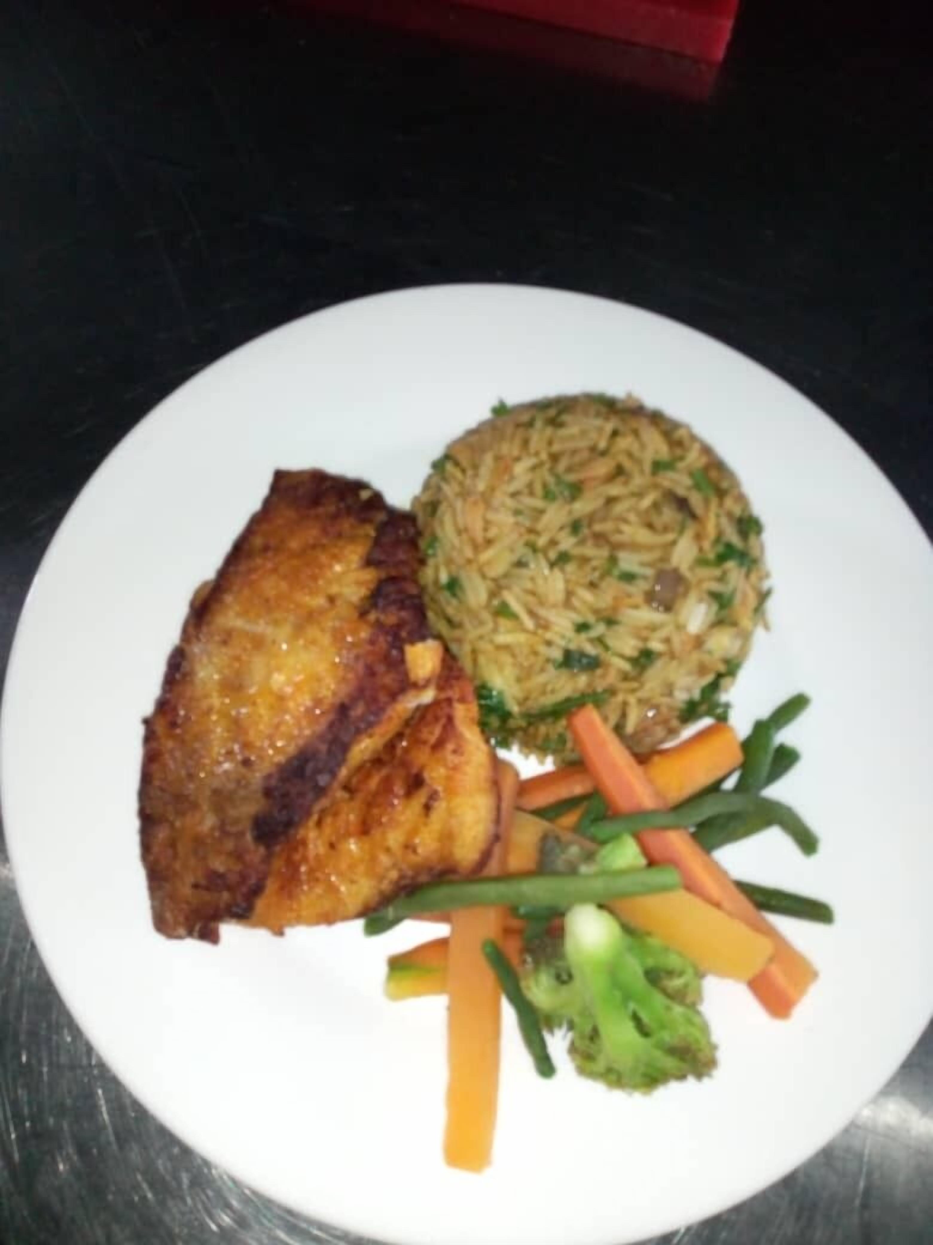Une assiette contenant un morceau de viande grillée, une portion de riz et un mélange de légumes, notamment des carottes et des brocolis.