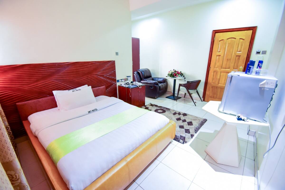 Une chambre d’hôtel avec un lit, un bureau avec un ordinateur, une chaise, un canapé, une petite table avec des fleurs et une porte.