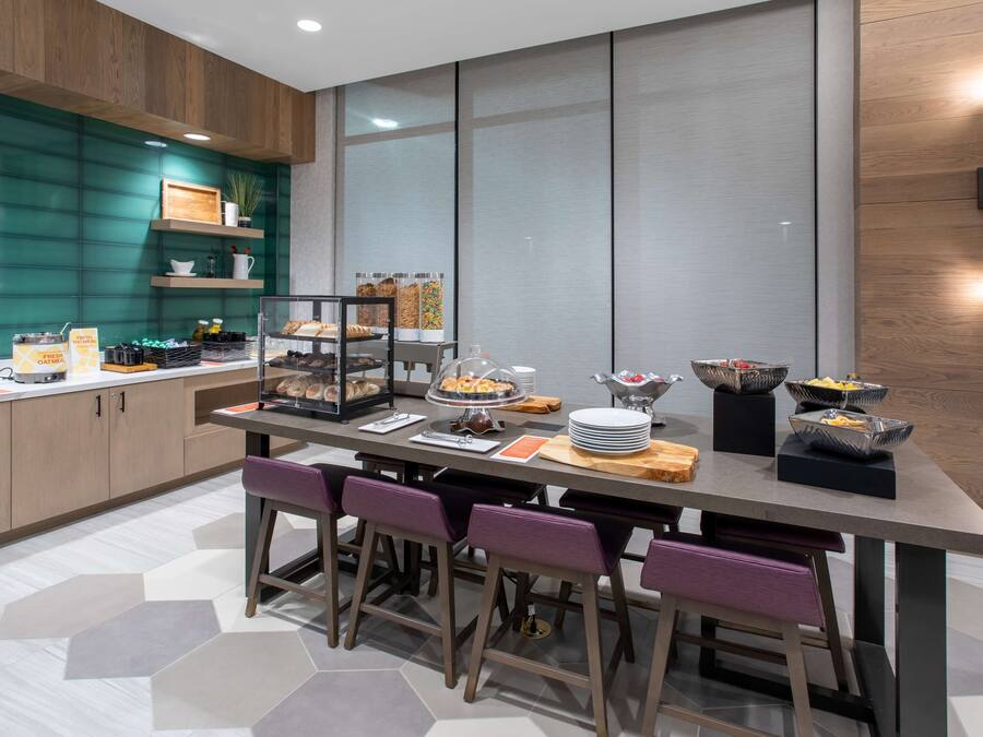 A modern kitchen with a breakfast bar, wooden cabinets, and a large window.