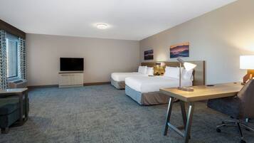 Quarto de hotel com cama grande, escrivaninha, cadeira, televisão e janela com cortinas.