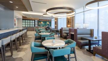 Een modern restaurant met ronde tafels en stoelen, een bar en een keuken op de achtergrond.