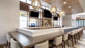 A modern bar area with a long counter, bar stools, a wine rack, and a television screen. - Hilton Garden Inn Albuquerque Downtown (Albuquerque)