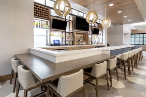 Un área de bar moderna con una barra alargada, taburetes, una estantería para vinos y una pantalla de televisión.