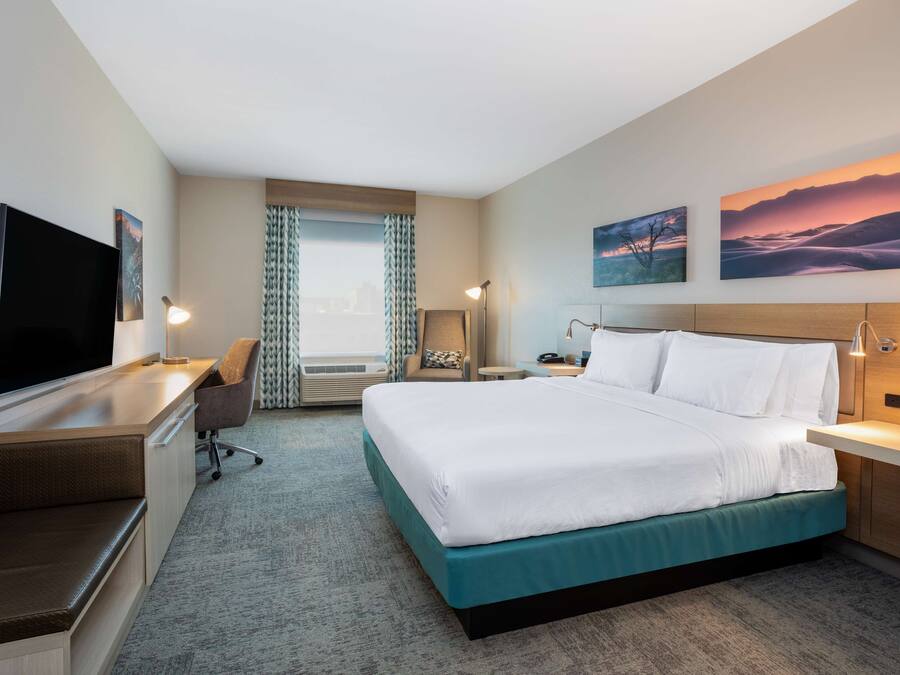 A hotel room with a bed, a desk, a TV, and artwork on the walls.