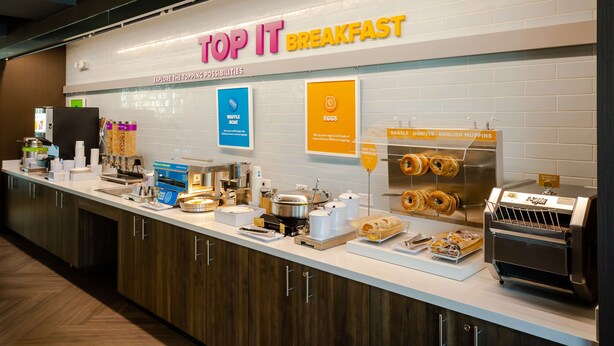Un comptoir où l’on sert le petit-déjeuner, avec une enseigne indiquant « Top It Breakfast » et une variété d’aliments exposés.