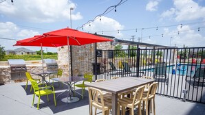 Une terrasse extérieure avec une table et des chaises, un parasol rouge et un barbecue.