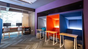 Un espace de bureau moderne avec un sol à motifs en chevrons, un bureau doté de deux écrans et un coin salon agrémenté de cloisons géométriques aux couleurs vives.