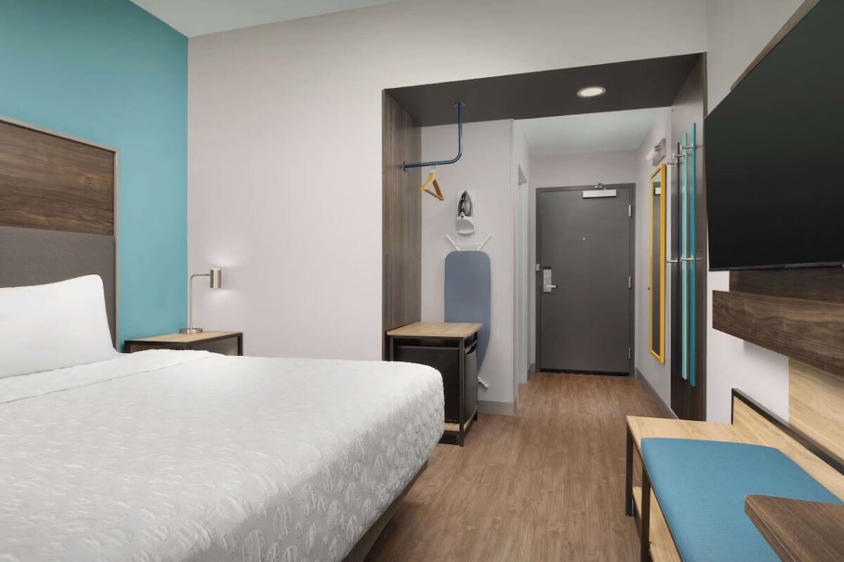 A modern hotel room with a large bed, a desk, a bench, and a wardrobe.