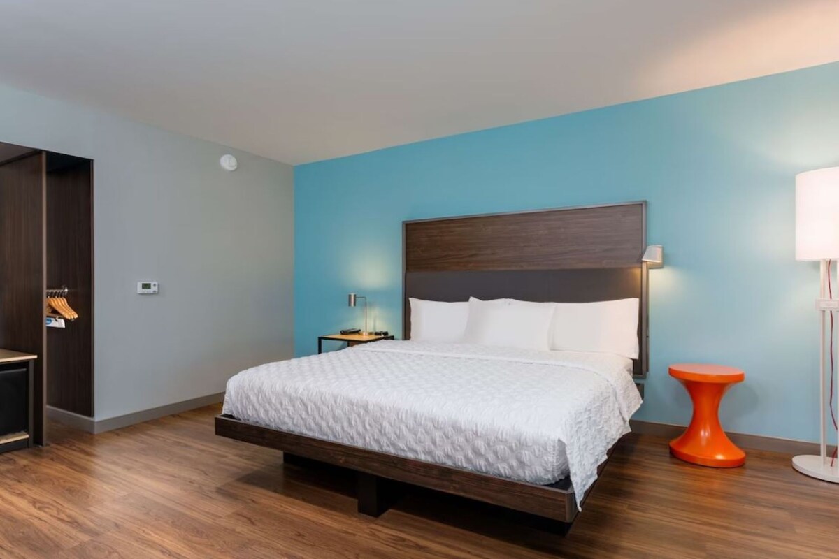 A modern bedroom with a bed, a nightstand, a wardrobe, and a unique orange side table.