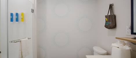 A bathroom with a glass shower door, a toilet, a sink with a towel dispenser, and a wall with a circular pattern.