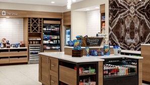 Un espacio comercial moderno con un mostrador que exhibe aperitivos y bebidas, estantes llenos de diversos productos, y un letrero que indica 'Specialty Items'.