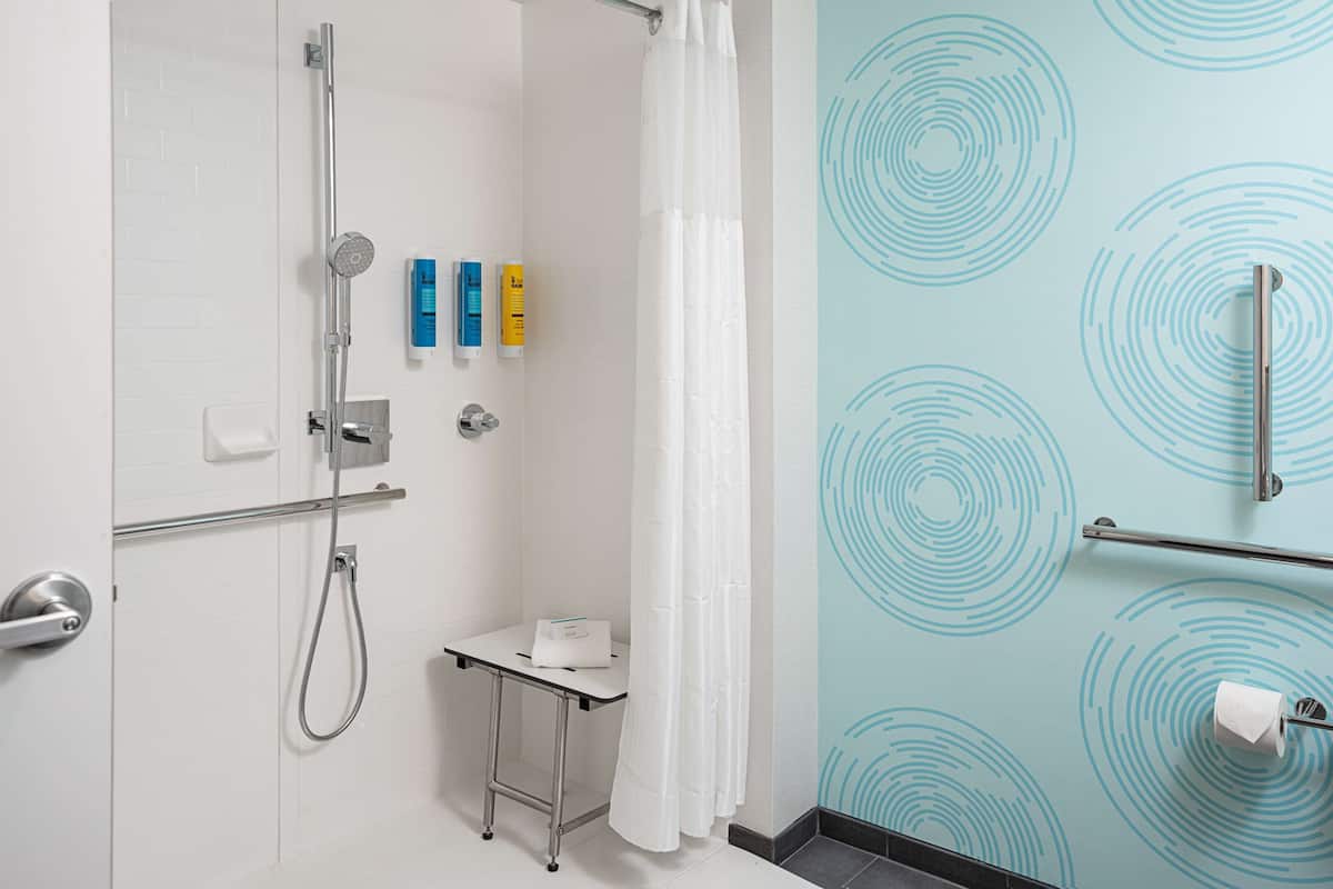 A bathroom with a shower, toilet, and a small table with toiletries.