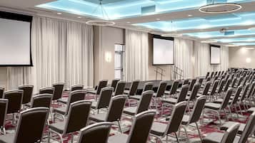 A conference room with rows of chairs, a large screen, and a carpeted floor.