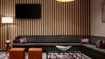 A modern living room with a sectional sofa, a glass coffee table, and a striped wall panel.