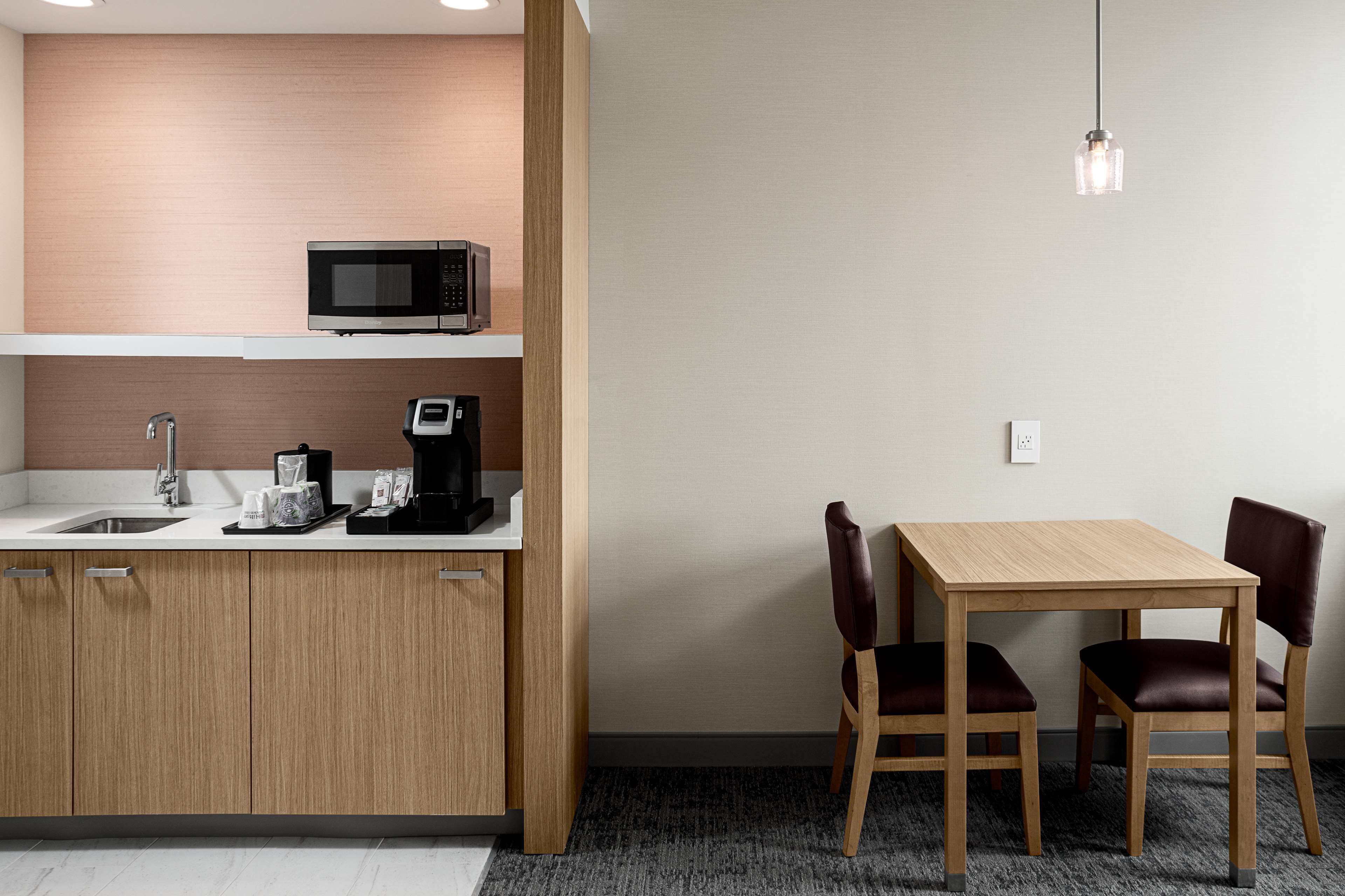 A compact kitchen with a microwave, coffee maker, and sink. There is a wooden table with two chairs.