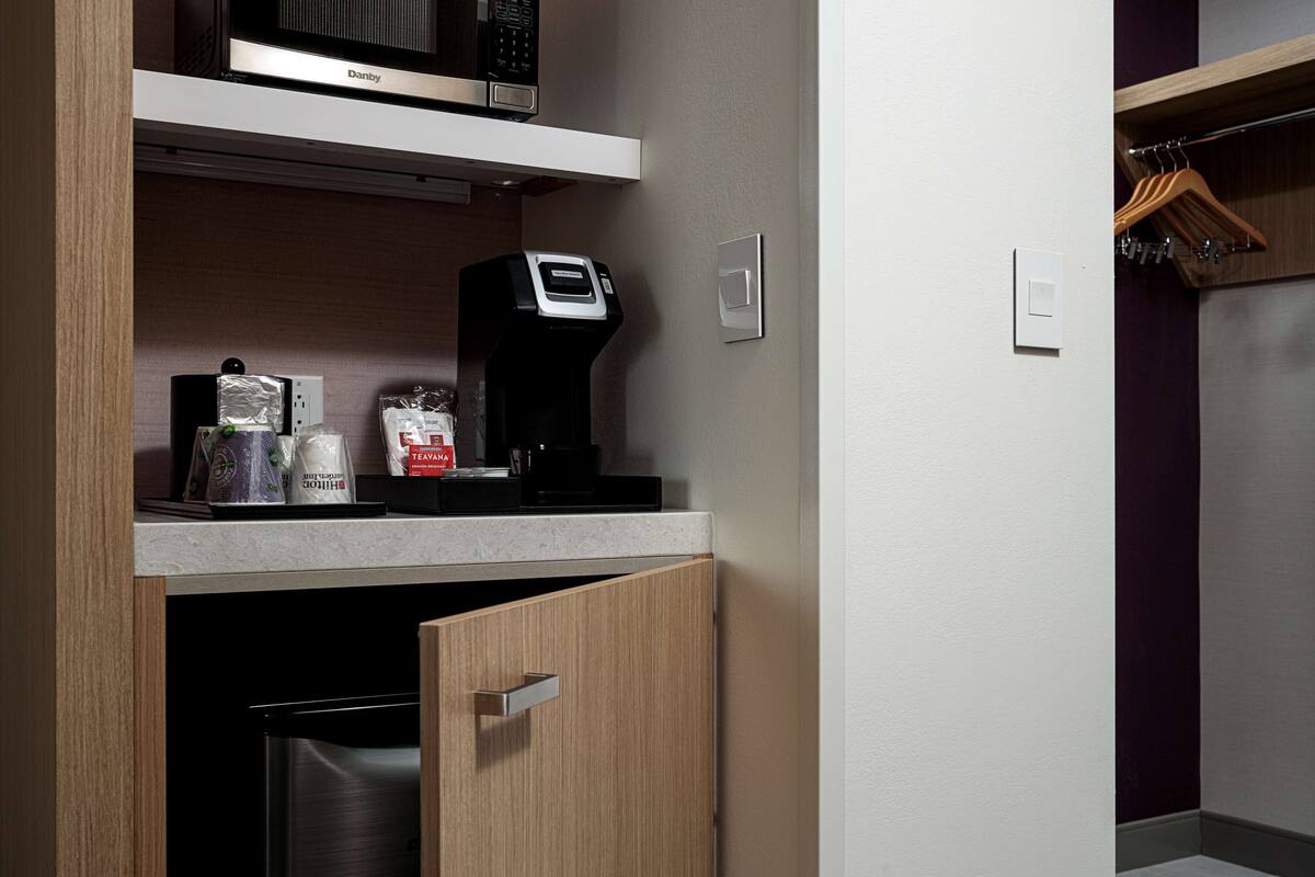 A compact kitchen with a microwave, coffee maker, and tea bags on the counter.