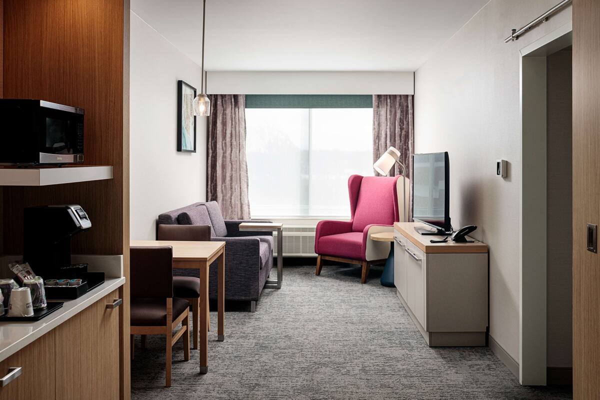 A compact hotel room with a kitchenette, a sofa, a desk, and a television.