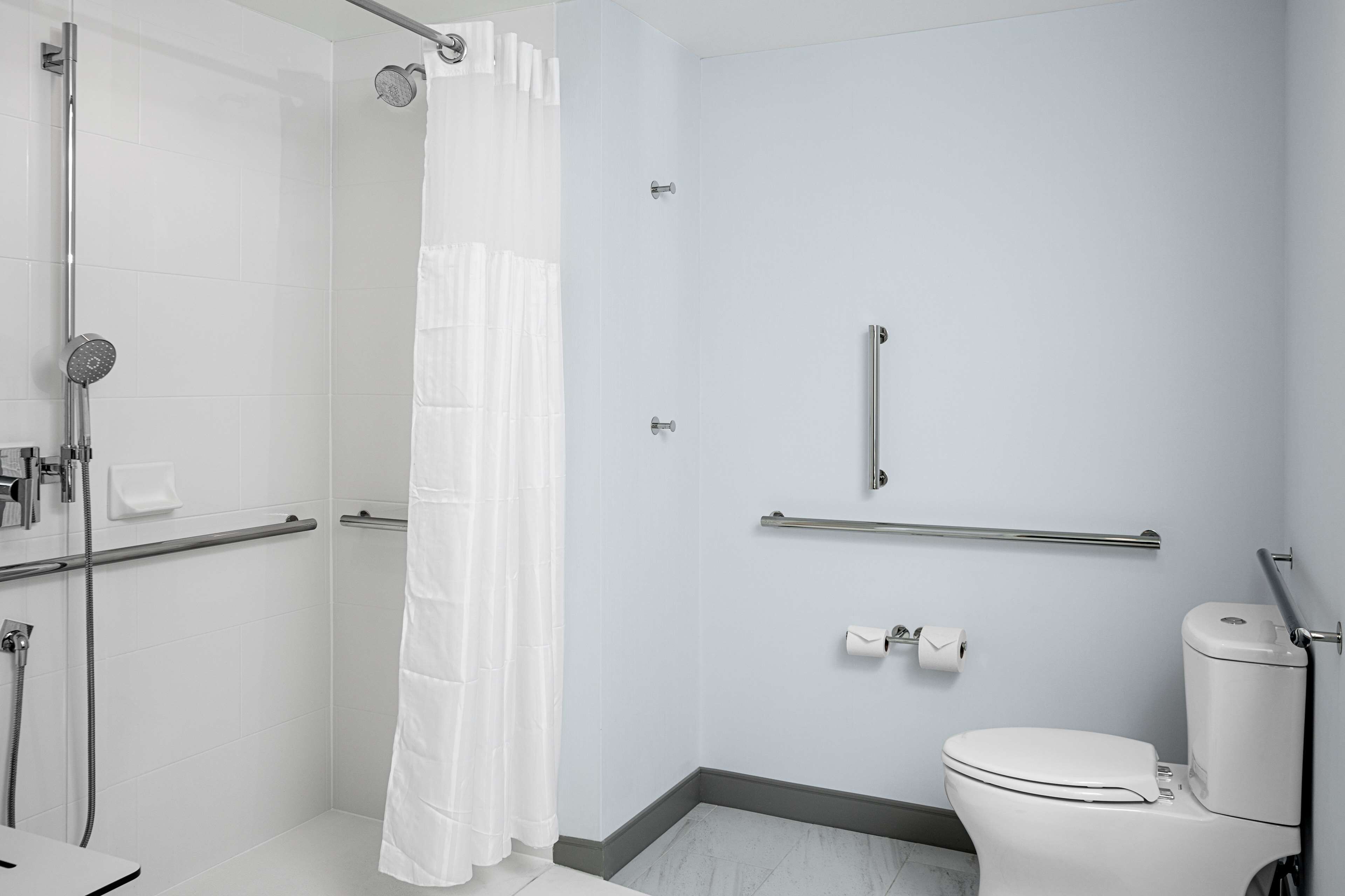 A modern bathroom with a shower, toilet, and grab bars.