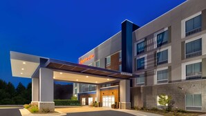 L'ingresso moderno di un hotel con una tettoia, una segnaletica con la scritta "Hampton Inn" e un cartello di benvenuto.