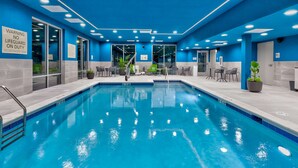 A swimming pool with blue tiles, surrounded by chairs and tables, and a sign warning no lifeguard on duty. - Hampton Inn Danville, VA (Danville)