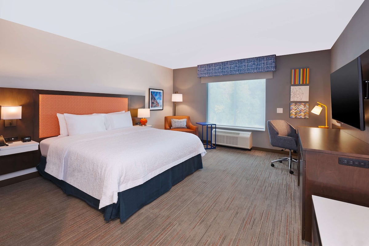 A hotel room with a large bed, a desk, a chair, a TV, and a window with a view.
