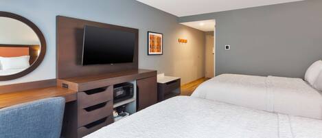 A hotel room with a bed, a desk with a flat-screen TV, a microwave, and a large mirror.