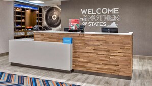 Una reception hotel con un cartello che riporta 'Welcome to the Mother of States', una parete in legno e un cartello blu 'Hilton Honors'.