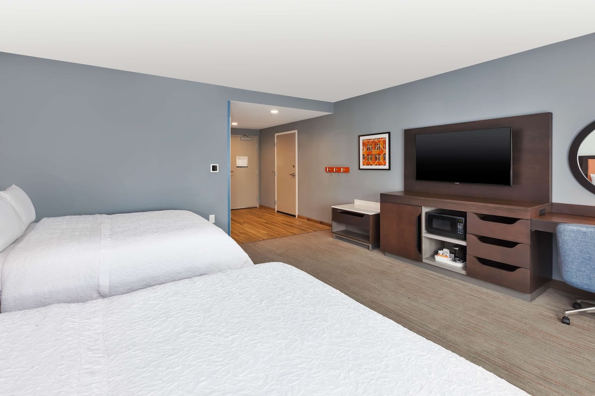 A hotel room with two beds, a TV, a desk with drawers, and a microwave.