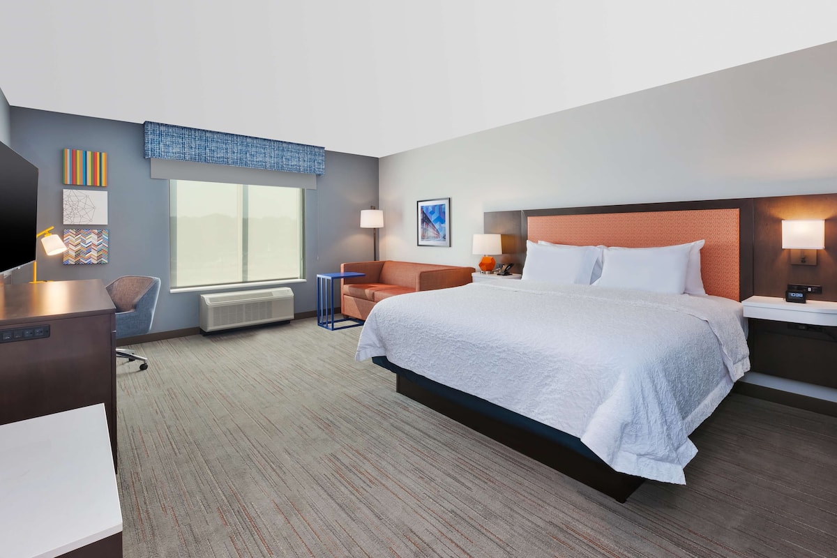 A hotel room with a large bed, a desk, a chair, and a window.