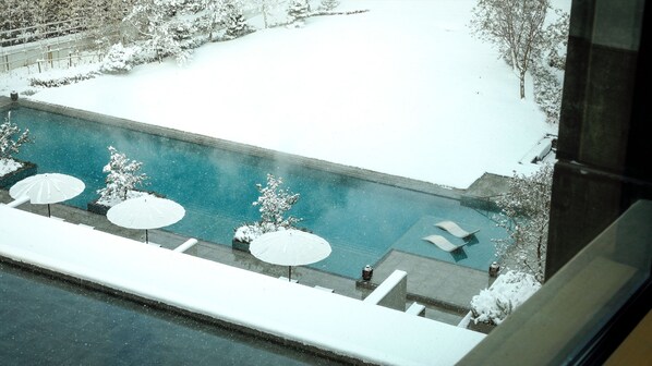 A view of a swimming pool with lounge chairs and umbrellas, surrounded by snow-covered trees and a fence. - ROKU KYOTO, LXR Hotels & Resorts (Kyoto)