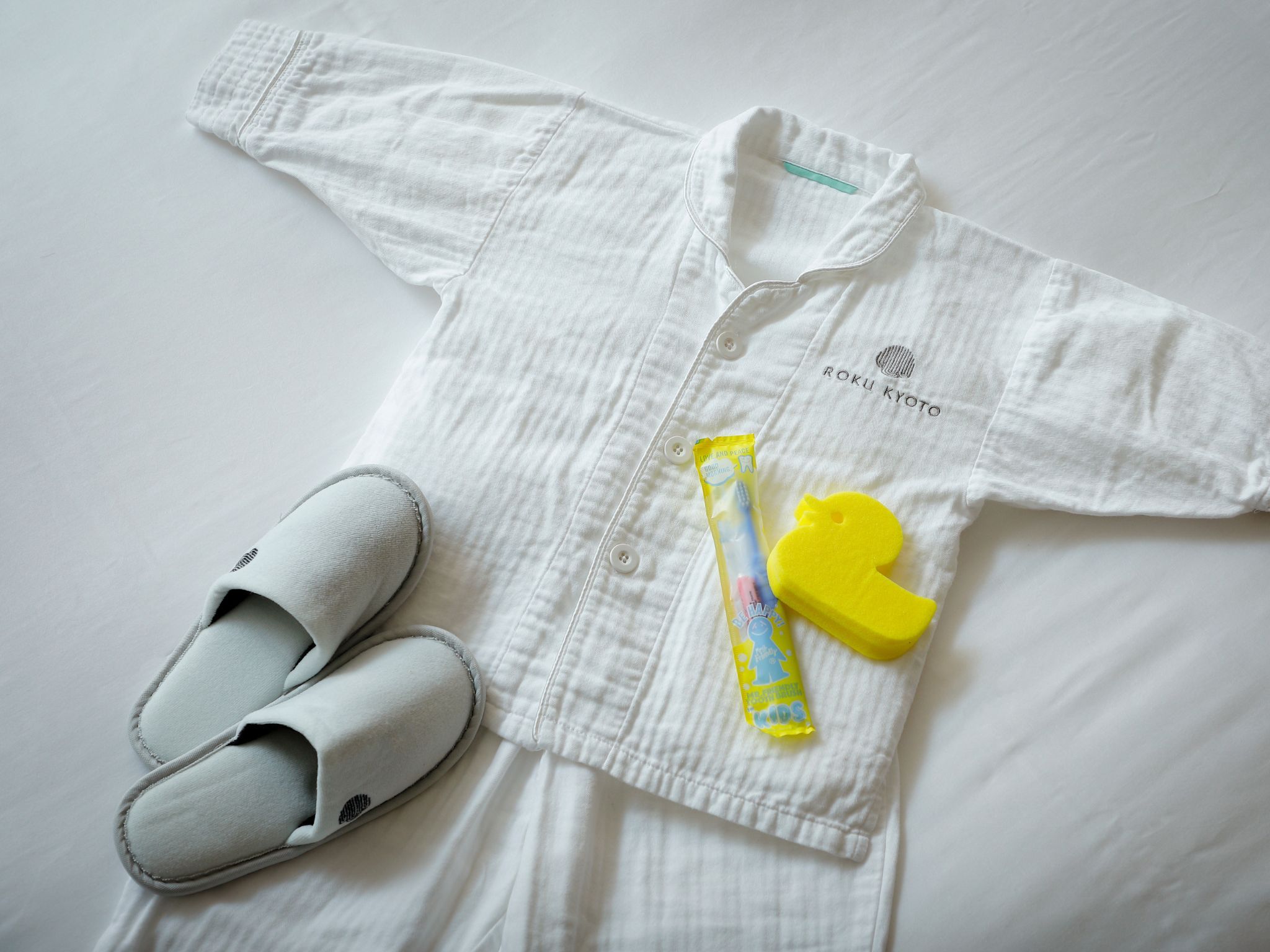 A white shirt with a logo, a pair of white slippers, and a yellow toy.