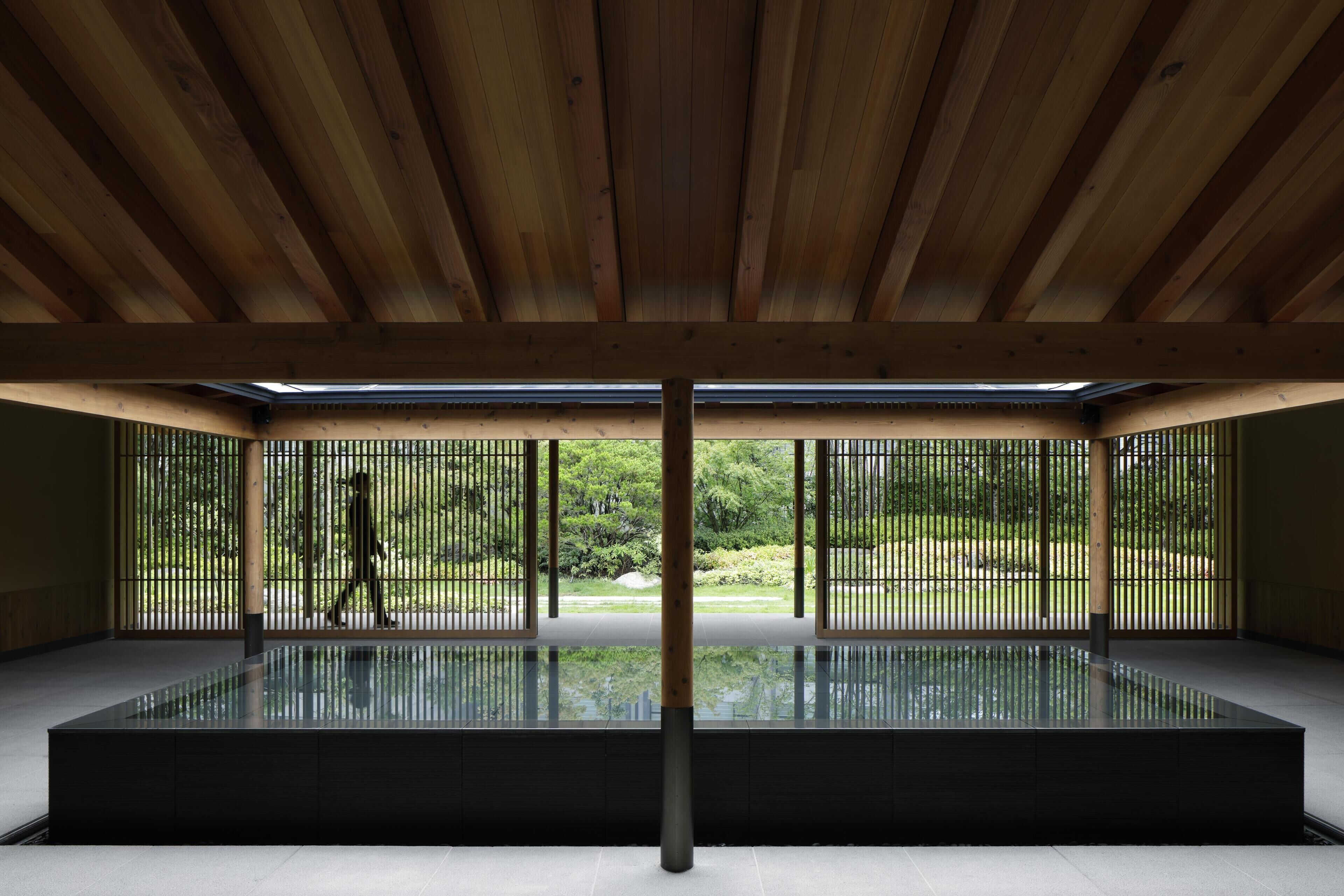 A room with a large glass pool, wooden ceiling beams, and a view of greenery through metal fences.