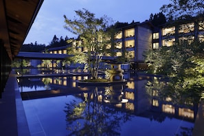 Un hotel moderno con una piscina reflectante, rodeado de árboles y edificios.