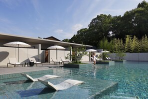 A swimming pool with lounge chairs and umbrellas, surrounded by trees and a modern building.