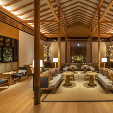 A spacious lobby with high ceilings, wooden beams, and a central seating area with round tables and sofas.