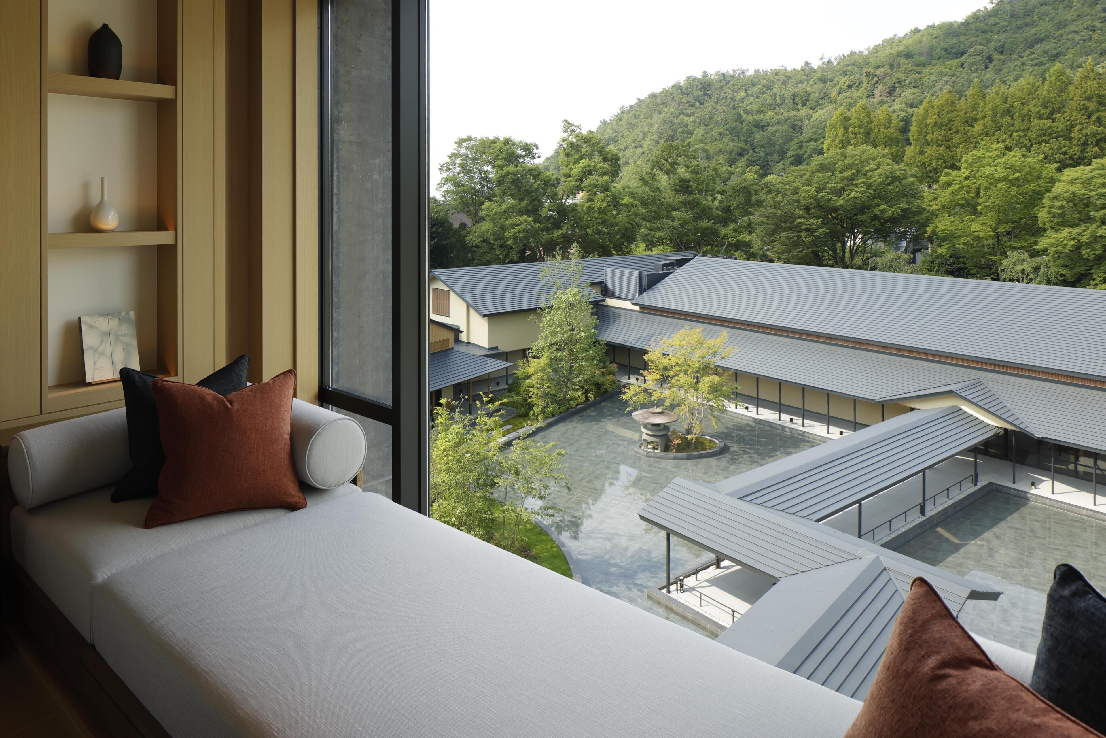 A modern room with a large window, a sofa, and a view of a courtyard with buildings and trees.