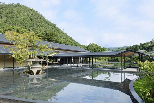 A modern building with a reflective pool, surrounded by greenery and a hilly backdrop. - ROKU KYOTO, LXR Hotels & Resorts (Kyoto)