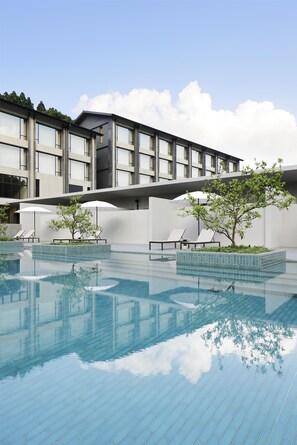 A modern building with a swimming pool, lounge chairs, and umbrellas.