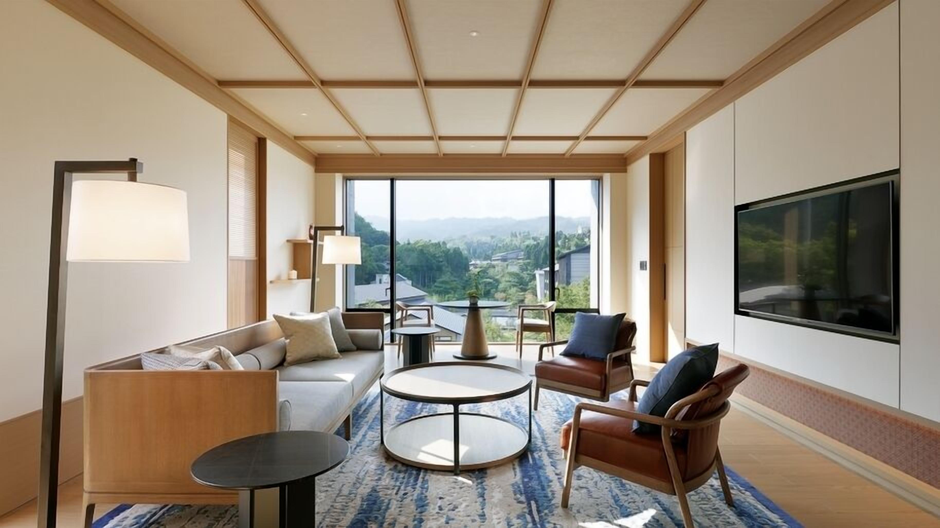 Een moderne hotelkamer met een bank, stoelen, een klein tafeltje, een televisie en een groot raam met uitzicht.