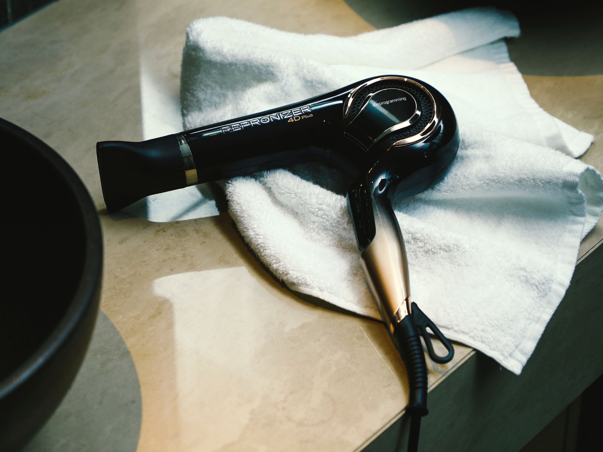 A hair dryer with a cord, placed on a white towel on a countertop.