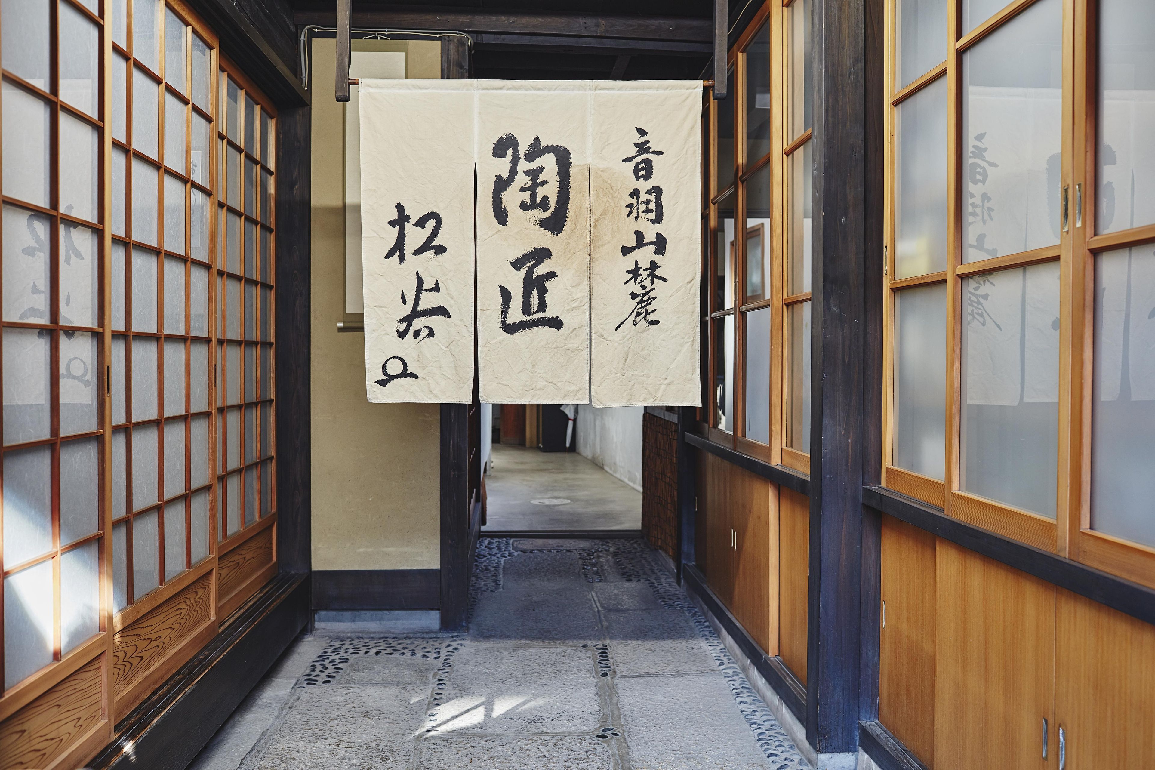 En gang med traditionelle japanske skydedøre og en ophængt rulle med japanske skrifttegn.
