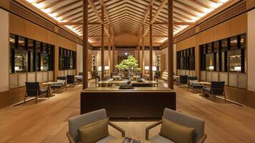 Un intérieur spacieux avec un plafond haut, des poutres en bois et un espace de détente central agrémenté d’une table et de chaises.