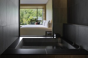 Une salle de bain moderne avec une grande baignoire, une petite table de chevet et une vue sur une chambre à coucher avec un lit et une fenêtre.