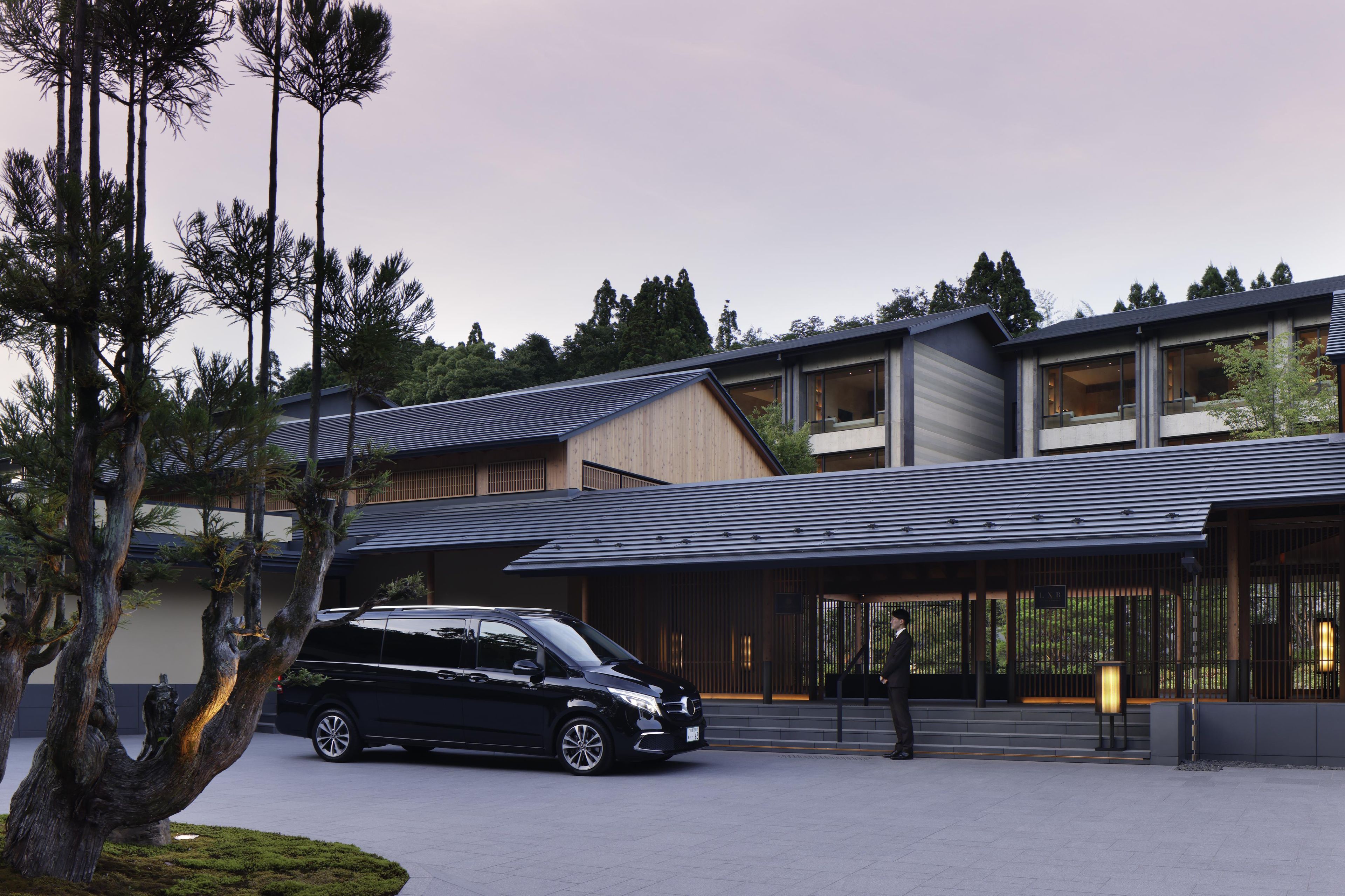 A modern building with a sloped roof, large windows, and a black car parked in front.