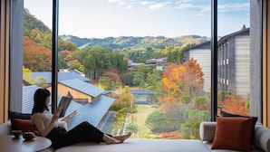 A room with a large window offering a view of a residential area with houses and autumn foliage.