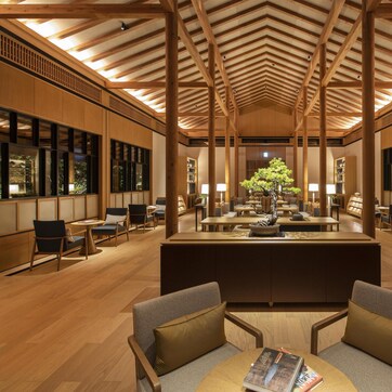 A spacious lobby with wooden beams, a central reception desk, seating areas, and a large tree.