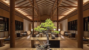 A traditional Japanese-style interior with a central bonsai tree, wooden beams, and a seating area with tables and chairs.